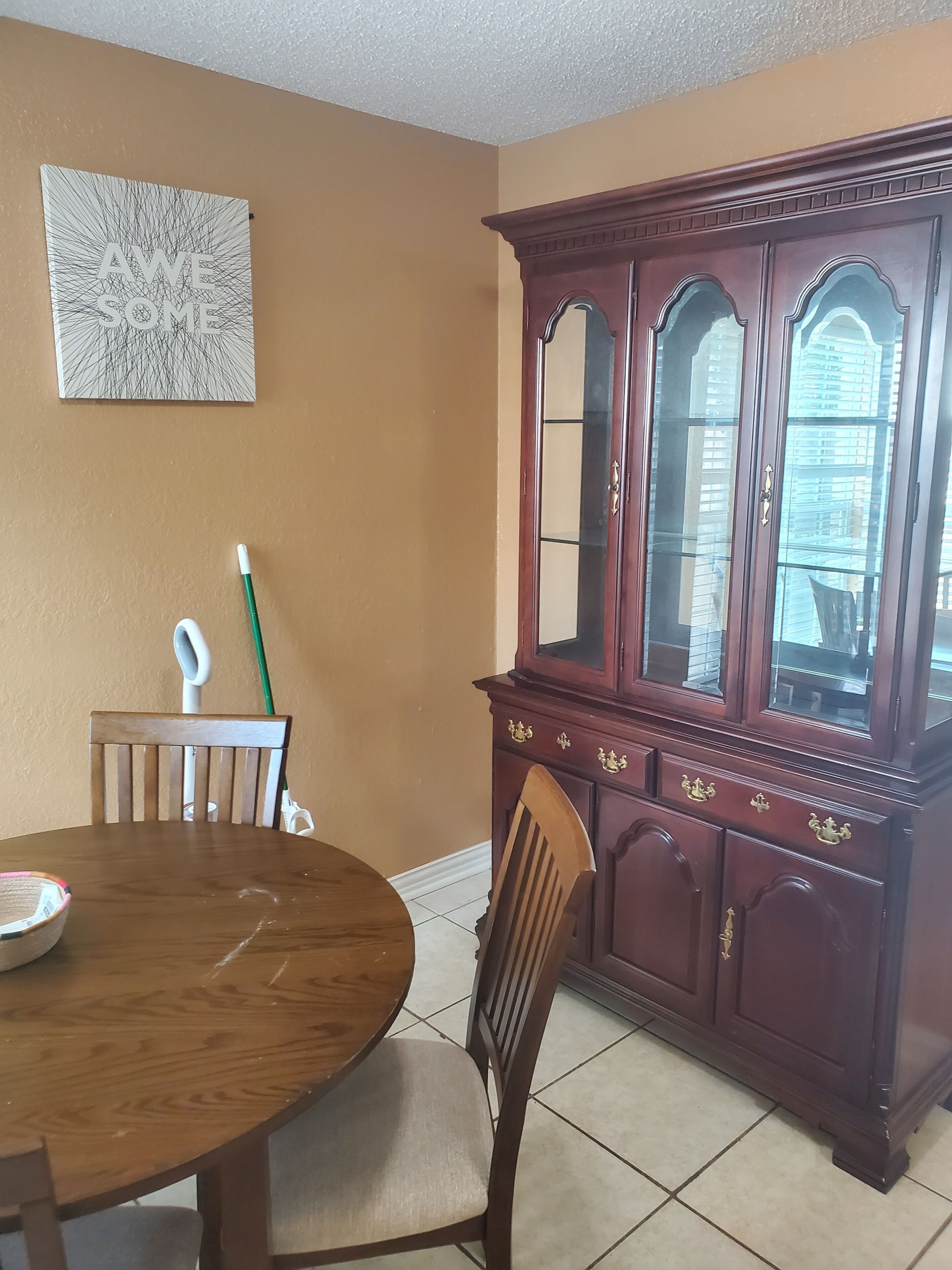 A dining area with a round table, chairs, a cabinet with glass doors, and a wall-mounted artwork.