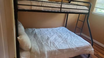 A bunk bed with a mattress and pillows, wooden flooring, and a window with blinds.