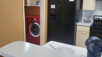 A kitchen with a refrigerator, washing machine, and a sink with a fan.