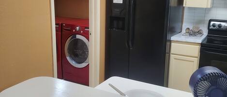Cocina equipada con refrigerador, lavadora y pileta con ventilador.