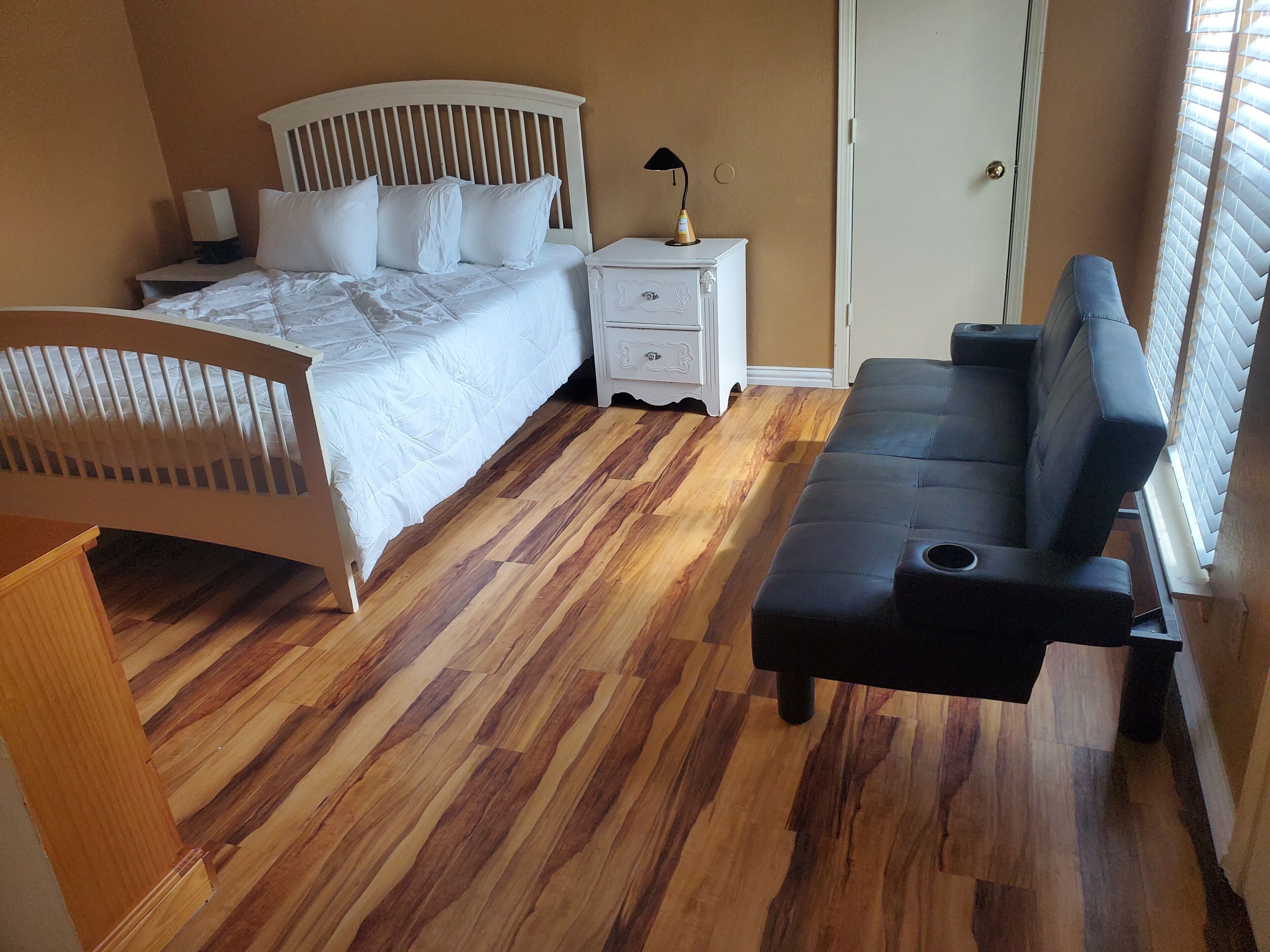 A bedroom with a bed, bedside table, lamp, and a sofa.