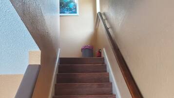 A wooden staircase with a handrail, a trash can, and a fire extinguisher on the wall.