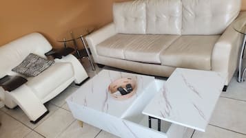 A living room with a white leather sofa, a patterned throw pillow, a glass coffee table, and a small side table.