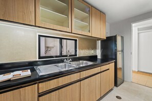 A kitchen with wooden cabinets, a black countertop, a stainless steel sink, and a black refrigerator. - Nevora by Kozystay - Kuningan (Jakarta Selatan)