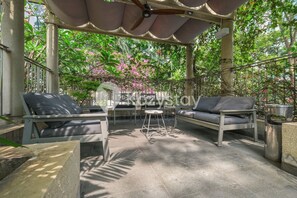 An outdoor seating area with two sofas, a small table, and a ceiling fan. - Nevora by Kozystay - Kuningan (Jakarta Selatan)
