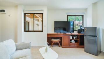 Un espacio habitable compacto con kitchenette, televisor de pantalla plana, refrigerador, sofá y una pequeña mesa con un florero.