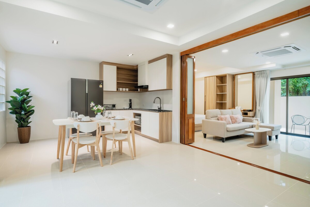 Une cuisine moderne avec des meubles blancs, un coin repas avec une table et des chaises blanches, et un salon avec un canapé et une table basse.