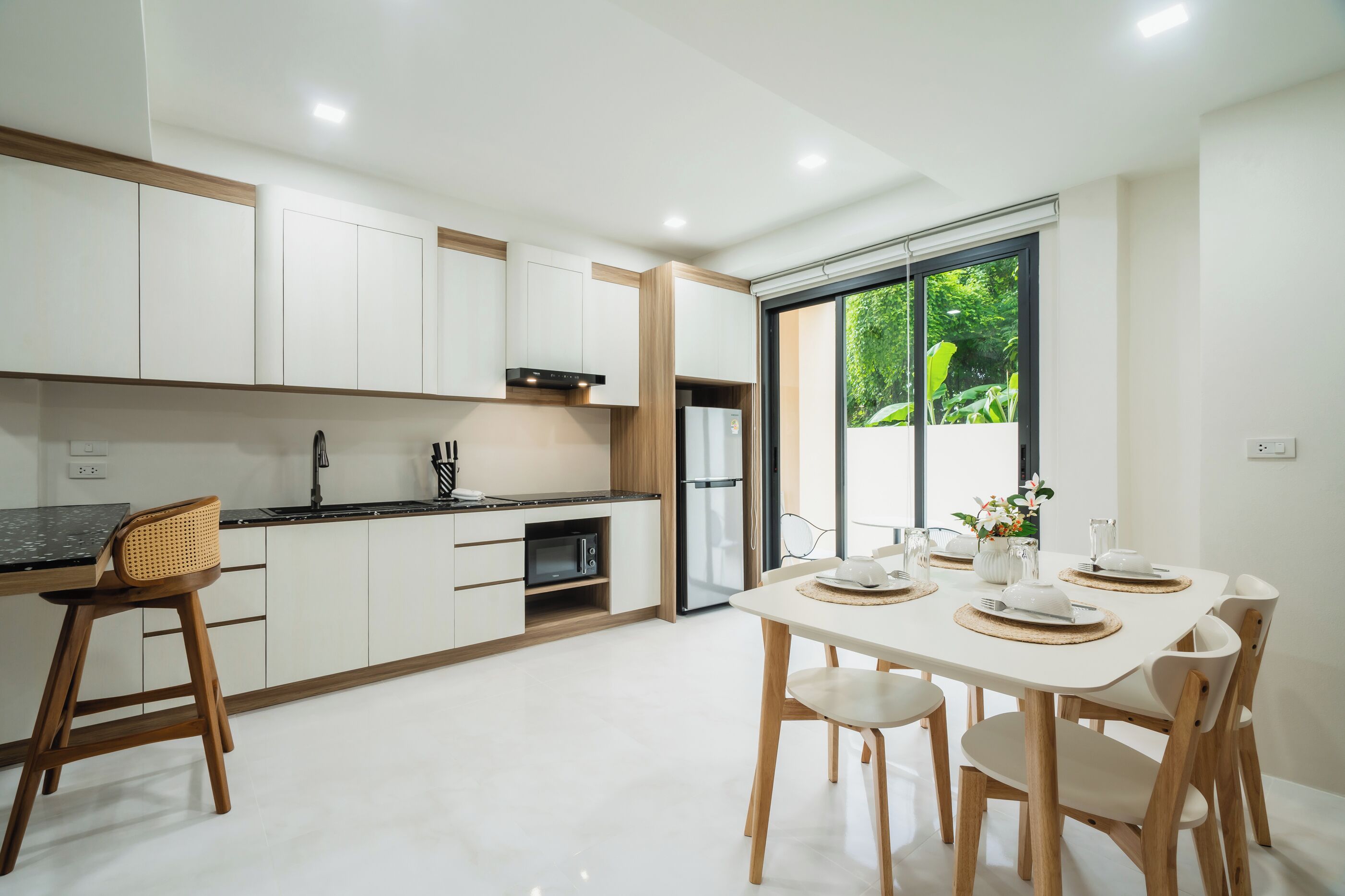 Una cocina moderna con armarios blancos, microondas integrado y comedor con una mesa dispuesta para dos.