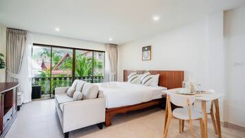 Habitación de hotel con cama, sofá, mesa de comedor con sillas y balcón con vistas a edificios y áreas verdes.