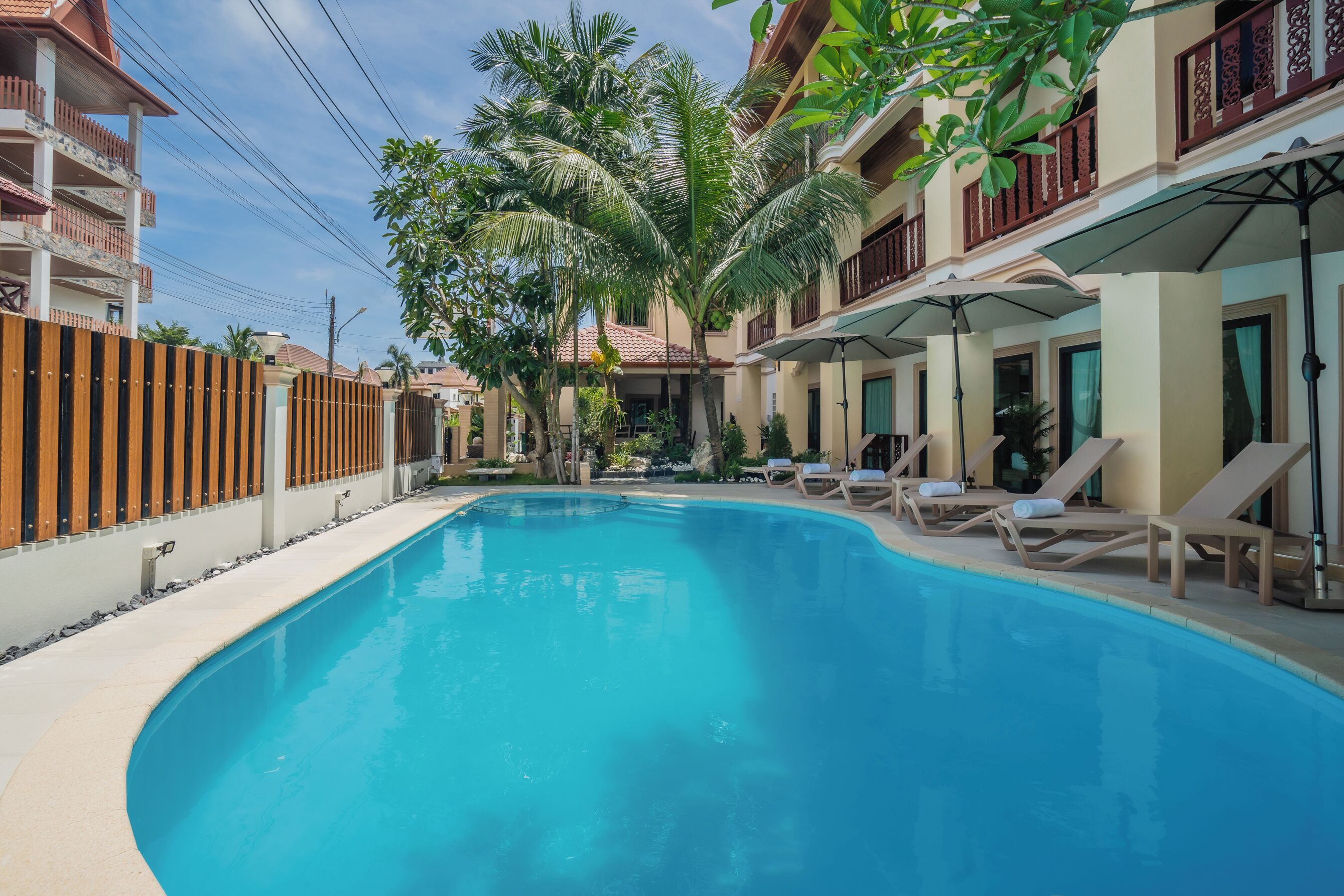 A swimming pool with lounge chairs and umbrellas, surrounded by buildings with balconies.