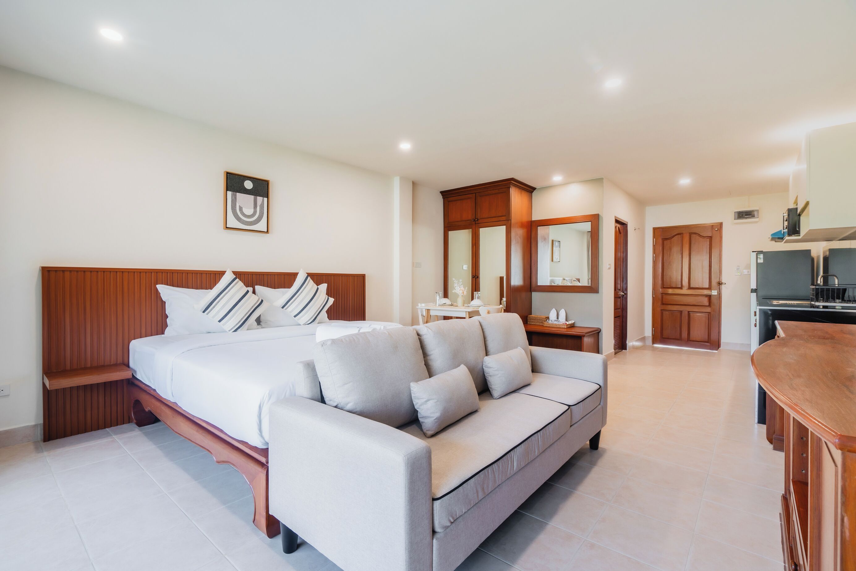 Habitación de hotel con cama, sofá, una mesita, espejo y kitchenette.