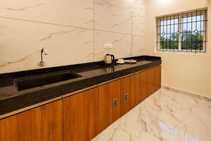 A modern kitchen with a marble countertop, wooden cabinets, a black sink, and a window with a view of greenery.