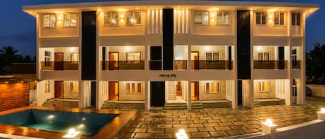 A multi-story building with a swimming pool and a well-lit exterior.