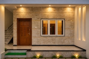A modern entrance with a marble wall, a wooden door, and a window with vertical blinds. - Gayathri Nest (Udupi)