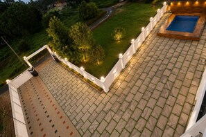 A rooftop terrace with a swimming pool, a paved area, and a view of the surrounding greenery.