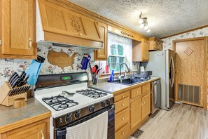 A kitchen with wooden cabinets, a gas stove, a stainless steel refrigerator, and a window with a view of trees. - Winter Getaway: Group Gatherings, Hunting, Hiking (Hancock)