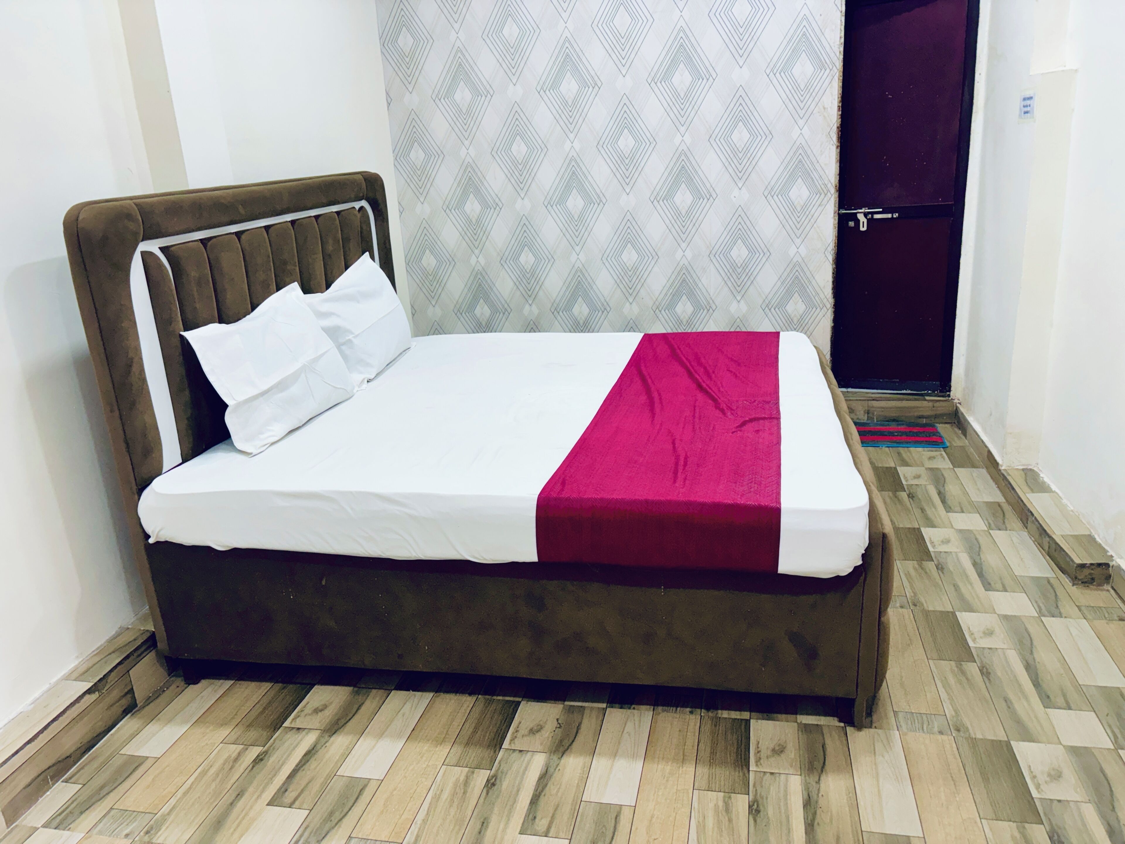 A bed with a headboard, white bedding, and a red blanket.