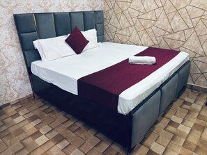 A bed with a dark headboard, white linens, a red throw, and a folded white towel. - Hotel Jhansi Grand Inn (Jhansi)