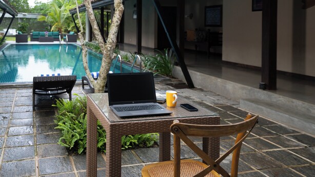 A laptop on a table with a chair, a yellow mug, and a smartphone beside it.