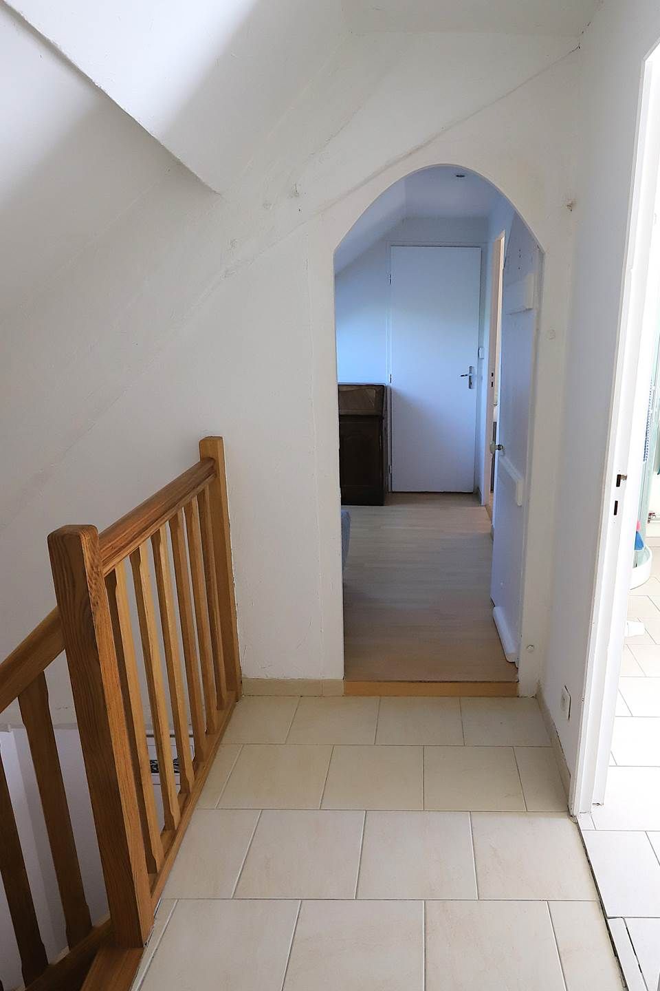 A corridor with a wooden railing, leading to a room with a door and a tiled floor.