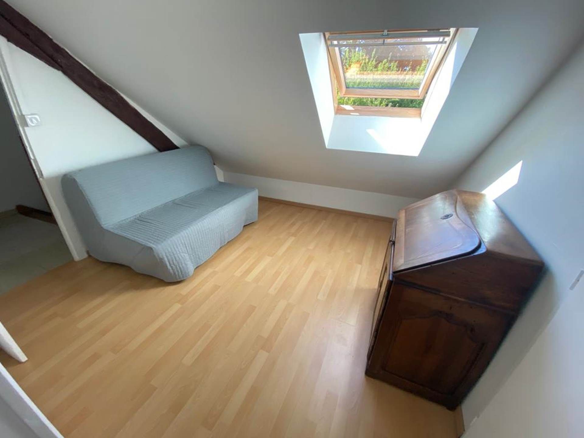 Une petite pièce avec un plafond en pente, une fenêtre, un canapé et un meuble.
