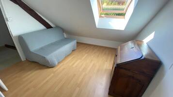 Une petite pièce avec un plafond en pente, une fenêtre, un canapé et un meuble.