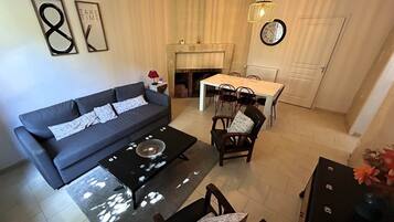 Een woonkamer met een bank, een eettafel met stoelen, een open haard en een klok aan de muur.