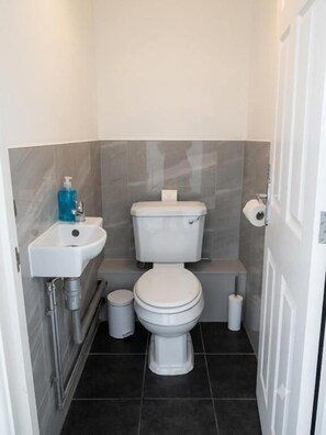 A small bathroom with a toilet, sink, and a trash bin. - Brigstock Luxe Stay Modern 2-Bed Apartment (Thornton Heath)