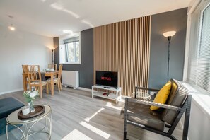 A modern living room with a flat-screen TV, a sofa with a yellow pillow, a dining area with a table and chairs, and a decorative vase on a side table. - Free Parking 2BR Sleeps 5 Close to JR Hospital (Headington)