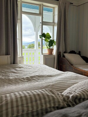 A bedroom with a large bed, a window with curtains, a potted plant, and a view of the outdoors. - Swiss-style farmhouse with fjord views (Bjoa)