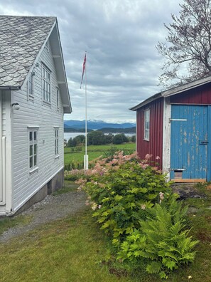 A house with a flagpole, a blue shed, and a grassy area with ferns. - Swiss-style farmhouse with fjord views (Bjoa)