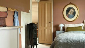 Quarto com cama, cômoda, porta para outro espaço e quadro na parede.