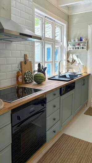 A kitchen with a built-in oven, a dishwasher, a wooden countertop, and a window with blinds. - Swiss-style farmhouse with fjord views (Bjoa)