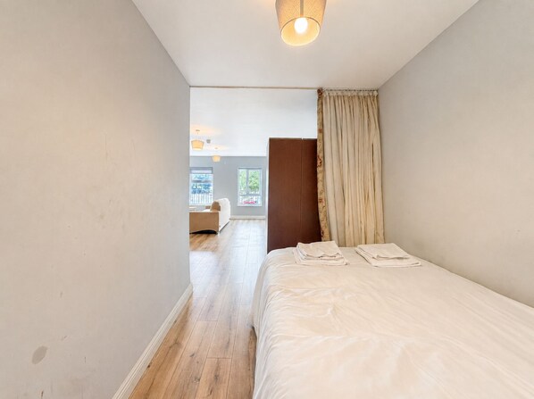 Un dormitorio con cama, suelo de madera, ventana y puerta que da a otra habitación.
