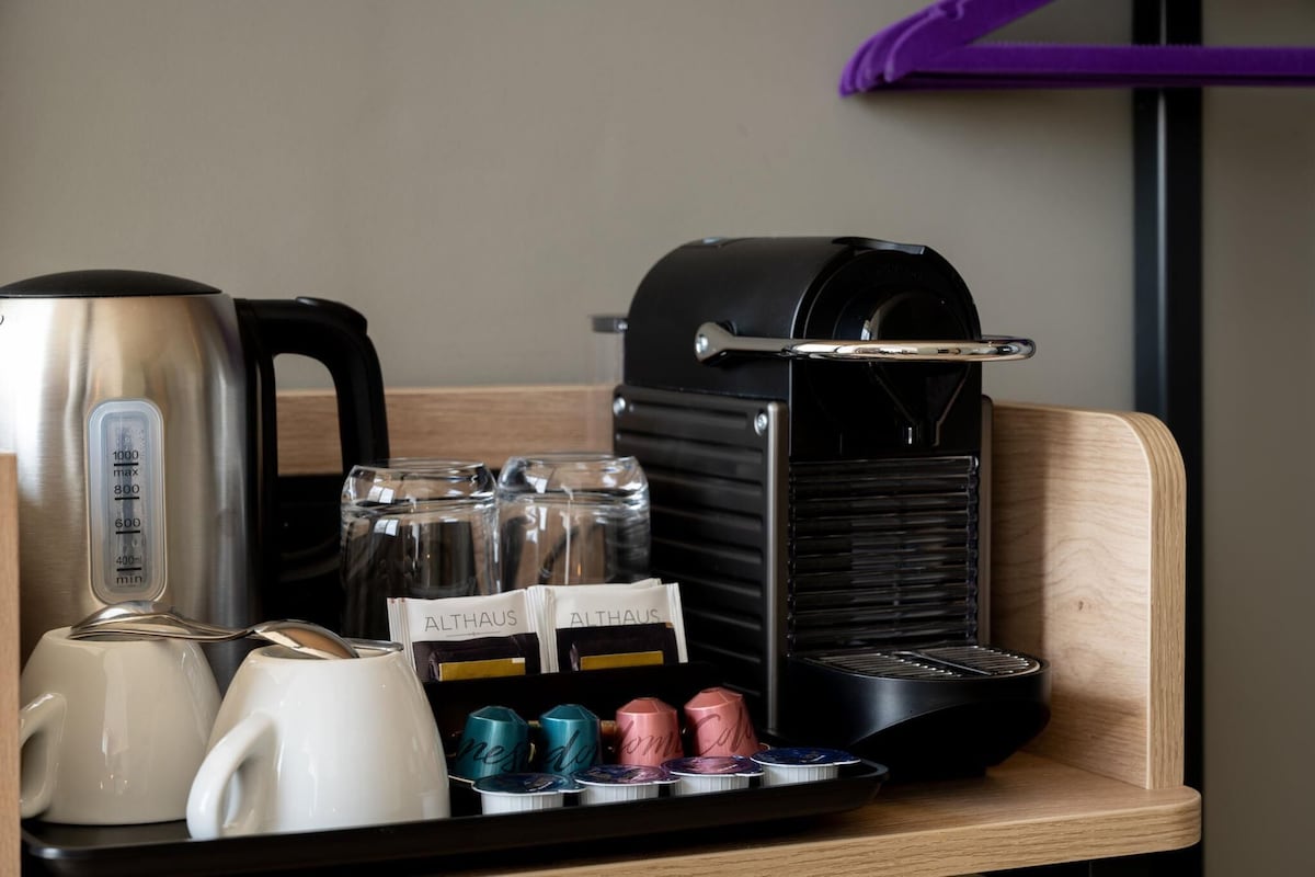 A coffee station with a coffee maker, a kettle, and a tray with coffee pods and a glass jar.