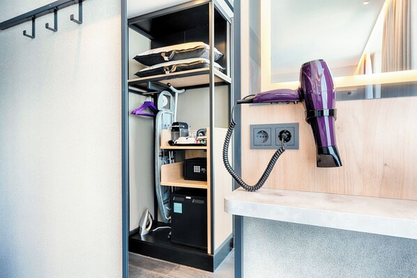 A compact room with a built-in wardrobe, a hairdryer on a wooden shelf, and a small desk area. - Premier Inn Mannheim City Quadratestadt (Mannheim)