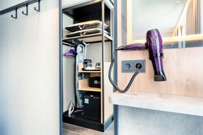 A compact room with a built-in hairdryer, a shelf with storage, and a window providing natural light. - Premier Inn Mannheim City Quadratestadt (Mannheim)