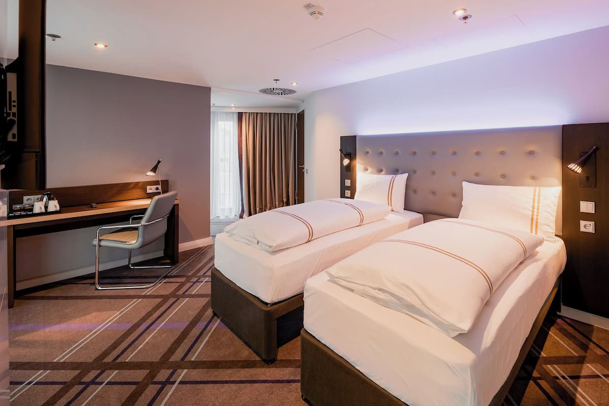 Ein Hotelzimmer mit zwei Betten, einem Schreibtisch, einem Stuhl und einer Dusche.