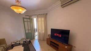 A living room with a television, a sofa, a coffee table, a patterned rug, a chandelier, and a door with curtains.