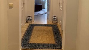 A hallway with a patterned rug, white walls, and a door leading to a room with a bed and curtains.