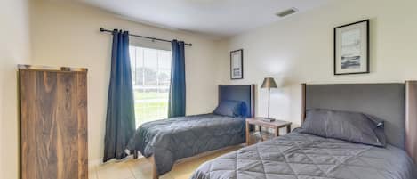 Une chambre avec deux lits, une armoire, une table de chevet avec une lampe et une fenêtre avec des rideaux.
