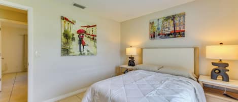 A hotel room with a bed, two bedside tables with lamps, a door leading to another room, and two paintings on the walls.