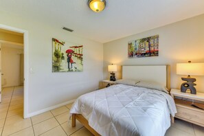 Een hotelkamer met een bed, twee nachtkastjes met lampen, een deur naar een andere kamer en twee schilderijen aan de muur.