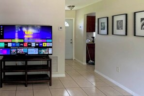 A living room with a flat-screen TV on a wooden stand, a hallway leading to a kitchen, and framed pictures on the wall. - 6 Mi to Dtwn! Centrally Located Sarasota Home (Sarasota)