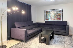 Un soggiorno moderno con un divano componibile, un tavolino, una lampada da terra e un grande quadro astratto appeso al muro.