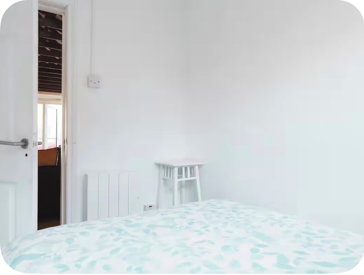 A room with a bed, a white chair, and a door leading to another room.