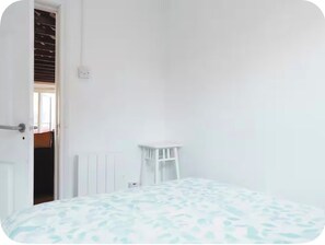 A room with a bed, a white chair, and a door leading to another room. - The Garden Lodge | Private Gated Historic Property (South Croydon)