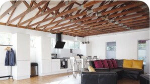 A spacious living area with a wooden ceiling, a black leather sofa, and a kitchen in the background.