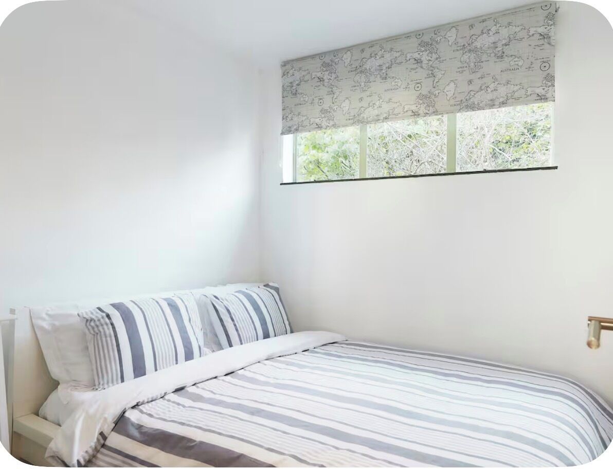 A bedroom with a single bed, a window with a world map curtain, and a plain white wall.