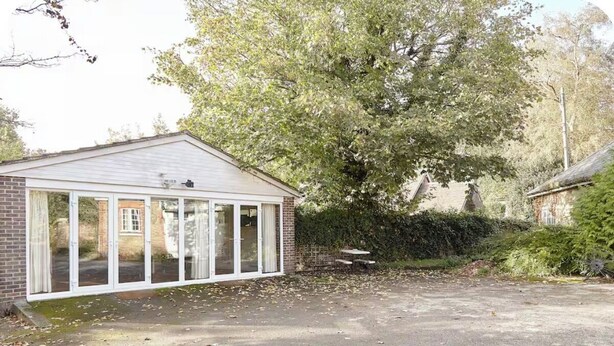 A single-story building with a garage door, a brick wall, and a large tree in the background.